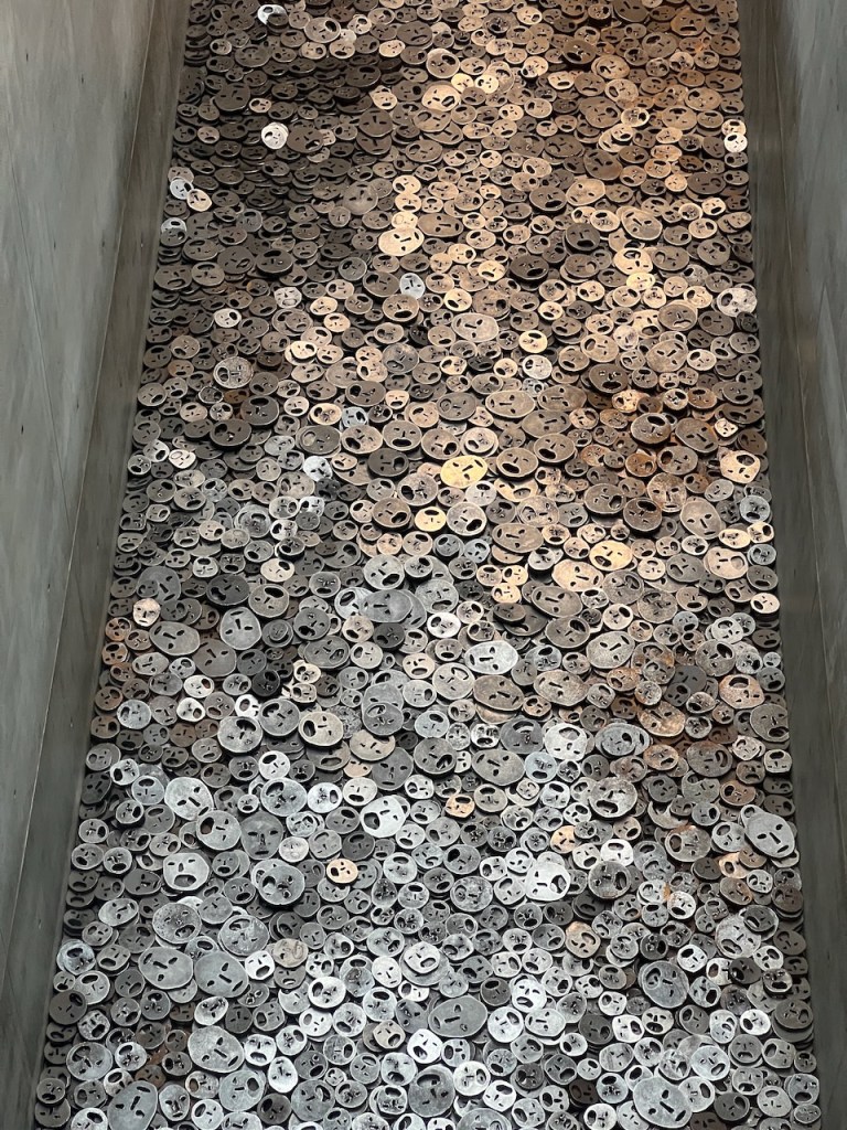A close-up view of numerous metallic discs resembling faces, scattered on a surface, creating a visually striking pattern.